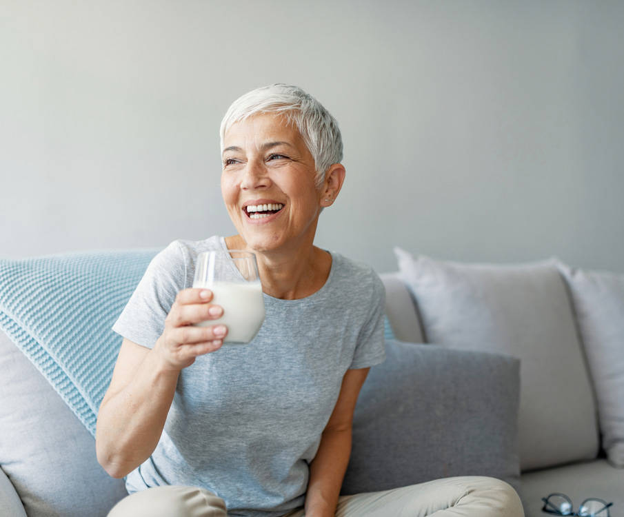 Glimlachende vrouw zit thuis op de bank en drinkt medische voeding uit een glas